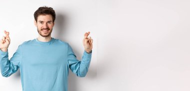 İyimser gülümseyen adam şans diliyor, dilek diliyor ve sonuçları bekliyor, beyaz arka planda duruyor..