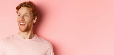 Kızıl saçlı ve sakallı yakışıklı beyaz adamın yakın çekimi, mutlu bir gülümsemeyle sola bakıyor, tanıtım teklifini kontrol ediyor, pembe arka planda duruyor..