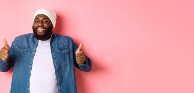 Tatmin olmuş yakışıklı siyah adam mutlu görünüyor, başparmak işareti yapıyor ve gülümsüyor, onaylıyor ve övüyor, tavsiye ediyor, pembe arka plan.