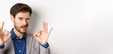 Kendine güveni tam yakışıklı bir adama yaklaş, iyi işaretler göster ve kameraya göz kırp, jest yap, beyaz arka planda dur..