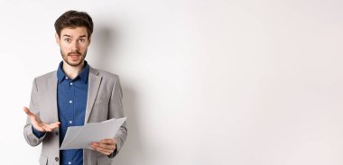 Kafası karışmış işadamı kötü belgeye bakıyor, anlaşmadan şikayet ediyor, kağıt üzerinde hayal kırıklığına uğramış, beyaz arka planda takım elbise içinde duruyor..