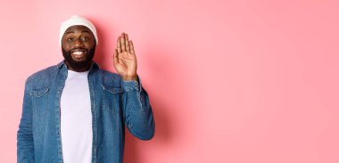 Dostça gülümseyen siyah adam merhaba diyor, el sallıyor, seni selamlıyor, pembe arka planda duruyor..