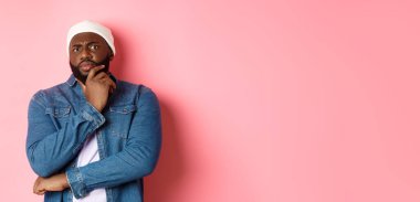 Şüpheci Afrikalı Amerikalı adam kameraya şüpheyle bakıyor, şüpheci duruyor ve düşünüyor, pembe arka plan.