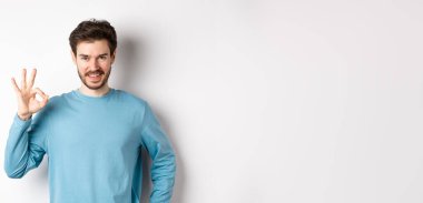 - Tamam. Yakışıklı gülümseyen adam iyi bir işaret veriyor ve kendinden emin görünüyor, iyi bir şey tavsiye ediyor veya övüyor, beyaz arka planda duruyor..