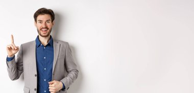 Heyecanlı takım elbiseli işadamı iyi fikir sunuyor, Eureka işaretinde parmağını kaldırıyor ve komik görünüyor, öneriler söylüyor, beyaz arka planda duruyor..