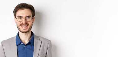 Gözlüklü, takım elbiseli, kameraya gülümseyen, beyaz arka planda mutlu görünen genç ofis çalışanlarının yakın çekimi..