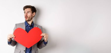 Adam, elinde büyük kırmızı kalp kesiği olan, beyaz arka planda Sevgililer Günü 'nde duran güzel birine hayret ediyor. Boşluğu kopyala