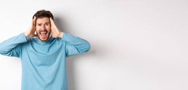 Beyaz arka planda duran, hayal kırıklığına uğramış ve bağıran, panik içinde çığlık atan genç beyaz bir adamın görüntüsü..