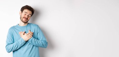 Yakışıklı genç adam romantik hissediyor, kalbi tutuyor ve güzel güzel anıları düşünüyor, beyaz arka planda duruyor..