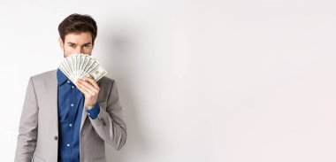 Takım elbiseli zengin bir işadamı. Para arkasında saklanıyor. Şehvetli bakışlarıyla kameraya bakıyor..