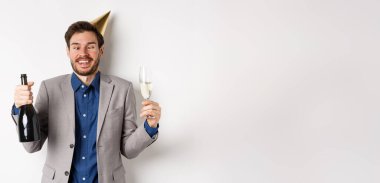 Kutlama ve tatil konsepti. Takım elbiseli komik sarhoş adam ve doğum günü şapkası, şaşı gözler ve partide eğlenmek, şampanya içmek, beyaz arka plan.