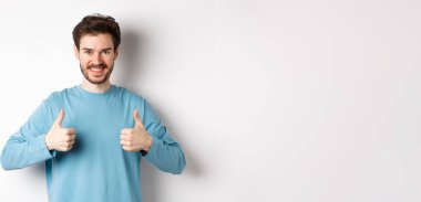 Gülümseyen yakışıklı adam iyi bir seçim yapıyor ve onaylıyor. Övüyor ya da tavsiye ediyor. Beyaz arka planda duruyor..