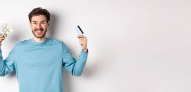 Mutlu adam gülümsüyor ve kredi kartını nakitle gösteriyor. Para ve temassız ödemeler arasında seçim yapıyor. Beyaz bir geçmişi var..