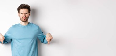 Surat asan adam kötü bir şeyi işaret ediyor, kaşlarını çatıyor ve şikayet ediyor, beyaz arka planda duruyor..