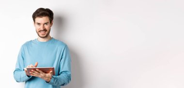 E-ticaret. Gülümseyen beyaz adam dijital tablet kullanıyor ve beyaz arka planda duran kameraya bakıyor..