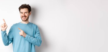 Fotokopi alanında reklam gösteren neşeli sakallı adam sol üst köşedeki logoyu işaret ediyor ve gülümsüyor, beyaz arka planın üzerinde duruyor..