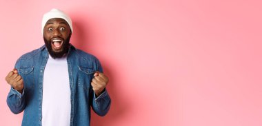 Şaşırmış ve mutlu adam kazanırken inançsızlıkla bakıyor, yumruklarını sıkıyor ve gülümsüyor şaşkınlıkla, zaferi kutluyor, amacına ulaşıyor, pembe arka planda duruyor..