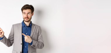 Takım elbiseli şüpheli bir girişimci solu kararsız bir suratla işaret ediyor, beyaz arka planda güvensiz duruyor..