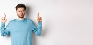 Hayal kırıklığına uğramış erkek model somurtuyor, olumsuz duygularla parmakla işaret ediyor, tanıtım teklifinden hoşlanmıyor, beyaz arka planda duruyor..