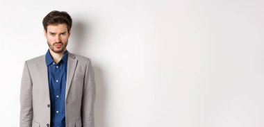 Üzgün adam somurtuyor, takım elbise giyiyor, haksız bir şey hissediyor, beyaz arka plana karşı çocuksu duruyor..