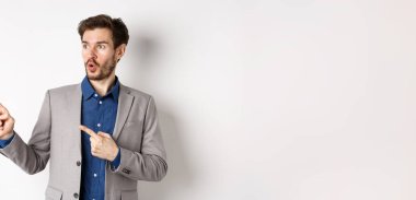 Vay canına, şuraya bak. Heyecanlı erkek yönetim kurulu başkanı sol parmaklarını işaret ederek logoya bakıyor, reklamını yapıyor, beyaz arka planda duruyor..