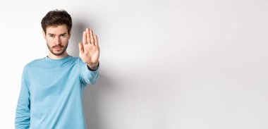 Ciddi genç adam elini uzatmış kendine güveniyor, dur diyor, kötü bir şeyi yasaklıyor ya da beyaz arka planda dikilip uyarı veriyor..