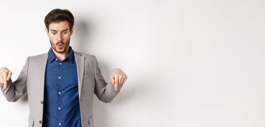 Vay canına, şuna bak. Etkilenmiş ve heyecanlı takım elbiseli işadamı, parmaklarını aşağı işaret ederek, beyaz arka planda duran şaşkın yüzüyle en alttaki reklama bakıyor..