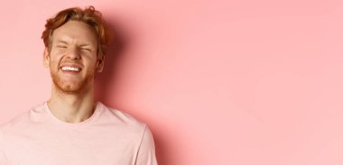 Kızıl saçlı, sakallı, gülen ve mutlu hisseden, pembe arka planda duran, eğlenen kaygısız bir adam..