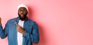 Kafası karışmış ve canı sıkkın Afro-Amerikan bir adam hayal kırıklığından korkup sol üst köşeyi işaret ediyor. Kötü reklam, pembe arka plan..