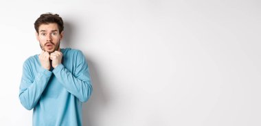 Korkudan titreyen korkmuş genç bir adamın görüntüsü, yüzünün yanında el ele tutuşmuş ve kameraya bakarken ürkmüş, beyaz arka planda duruyor..