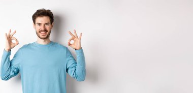 - Çok iyi. Gülümseyen yakışıklı iyi işaretler gösteriyor ve tatmin olmuş görünüyor, beyaz arka planda duruyor, mükemmel bir seçimi onaylıyor..