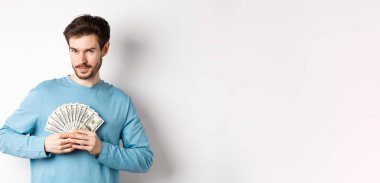 Kendine güvenen sakallı adam gülümsüyor, para gösteriyor ve kameraya bakıyor. Beyaz arka planda parası olan yakışıklı adam..