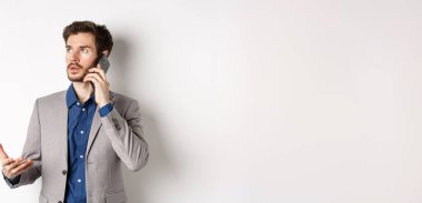 İş adamı telefonla konuşuyor, telefonla konuşuyor ve meşgul görünüyor, takım elbise giyiyor, beyaz arka plan.