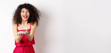 Tatiller ve kutlama konsepti. Kırmızı elbiseli, gülümseyen kadın sana mumlu doğum günü pastası veriyor, beyaz arka planda duruyor..