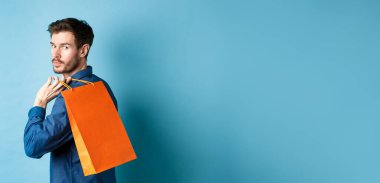 Arkaya bakan mutlu adam arkasını kolluyor ve mavi arka planda duruyor..