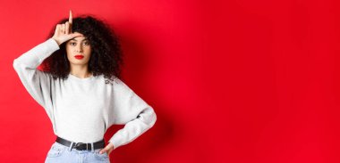 Kıvırcık saçlı, kendine güveni tam bir Avrupalı kadın, kayıp takımla alay ediyor, ezik jestleri yapıyor ve kameraya bakmıyor, kırmızı arka planda sıradan kıyafetler giyiyor..