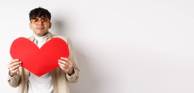 Tutkulu adam sevgililer gününde büyük kırmızı kalbi olan aşığı bekliyor. Romantik görünüyor ve aşkla beyaz arka planda duruyor..