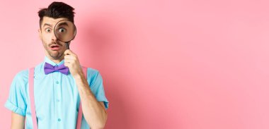 Komik adam şaşırmış yüzüyle büyüteçten bakıyor, ilginç bir şey görüyor, pembe arka planda duruyor..