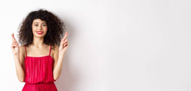 Umutlu, kıvırcık saçlı, şans dileyen, gülümseyen, dilek tutan, dua eden, beyaz arka planda duran güzel kız..