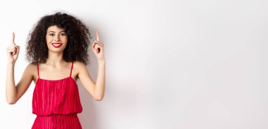 Zarif kırmızı elbiseli ve makyajlı, gülümseyen kadın, sevgililer gününde, beyaz arka planda duran ve tanıtım teklifini gösteren..