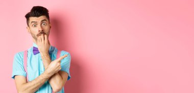 Papyonlu, cezbedici tırnaklarını yiyen, istediği bir şeyi işaret eden, pembe arka planda duran ilginç bir adam..