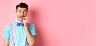 Gülümseyen bir adamın seçim yapması, hayalperest ve mutlu görünmesi, baştan çıkarıcı bir ifadeyle tırnağını yemesi, bir şey istemesi, pembe arka planda durması..