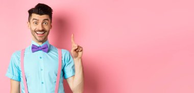 Neşeli beyaz adam bir fikir sunuyor, Eureka jestinde parmağını kaldırıyor ve gülümsüyor, çözüm öneriyor, pembe arka planda duruyor..