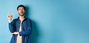 Yakışıklı bir adamın bir fikir sunduğu, parmağını kaldırdığı ve mavi arka planda durup düşünerek kafasını kaldırdığı bir görüntü. Boşluğu kopyala