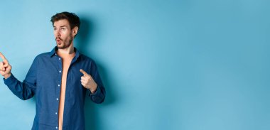 Sol üst köşeye bakıp işaret eden, reklamını yapan, mavi arka planda duran etkileyici adam..