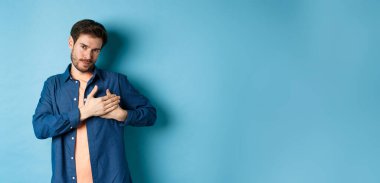 Romantik bir adam kalbi kucaklıyor ve gülümsüyor, teşekkür ediyor, mavi arka planda minnettar duruyor..