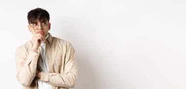 Üzgün ve yalnız genç adam üzgün yüzüyle boş alana bakıyor, beyaz arka planda düşünceli duruyor..