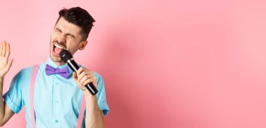 Parti ve festival konsepti. Komik adam şarkı söylüyor, mikrofonda kaygısız yüzüyle karaoke yapıyor, papyon ve pembe arka planda pantolon askısı takıyor..