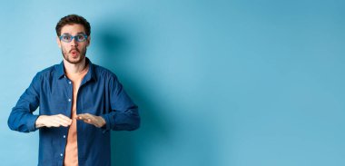 Gözlükçüde güneş gözlüğü deneyen, dans eden ve eğlenen, mavi arka planda duran komik adam..