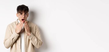 Şok olmuş görünen yakışıklı bir öğrencinin portresi, dedikoduları duyuyor ve inançsızlıkla bakıyor, elleri ile ağzını kapatıyor, beyaz arka planda duruyor..